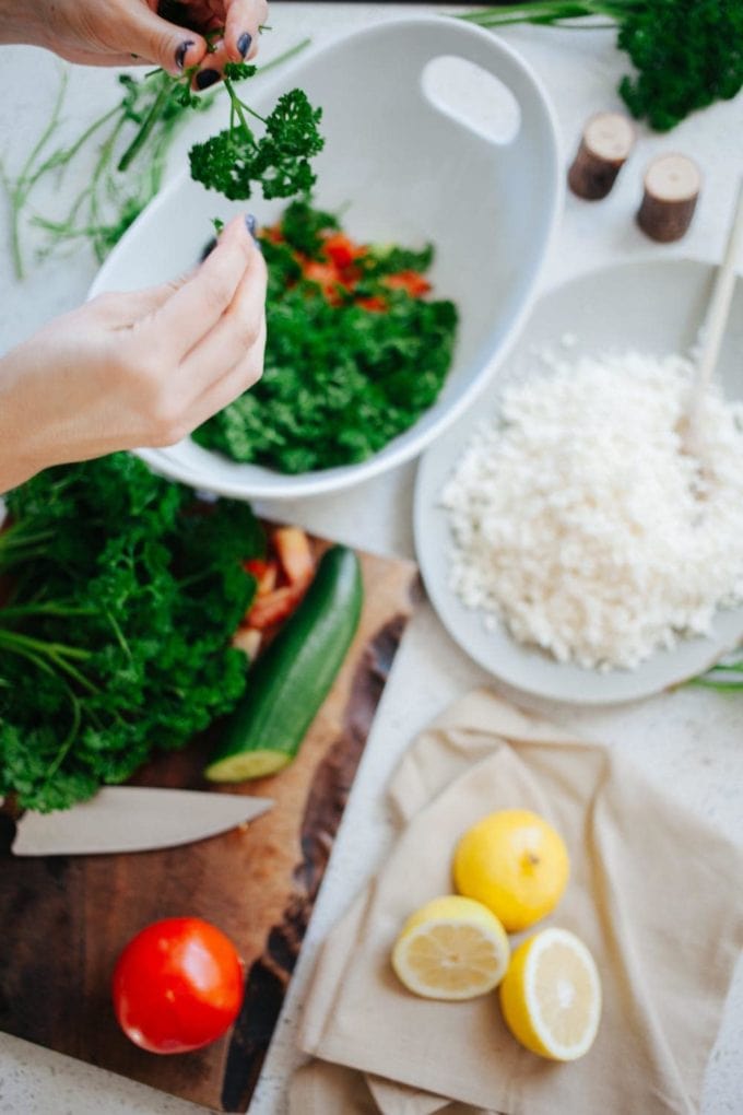 hands preparing parsley over bowls with cauliflower, lemons and tomato