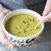 hand holding white bowl of greens soup