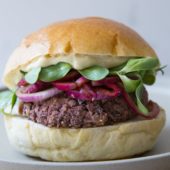 veggie burger on bun topped with mayo, sprouts and onions on a white plate