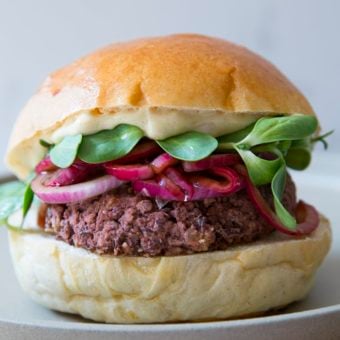 veggie burger on bun topped with mayo, sprouts and onions on a white plate