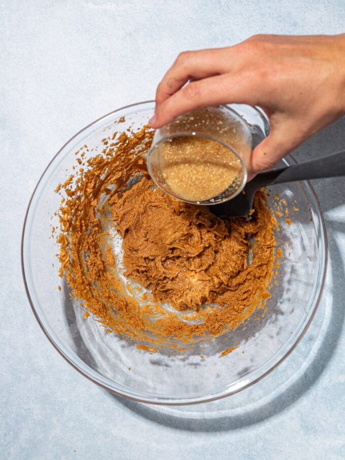 hand pouring flax egg into peanut butter mixture in bowl