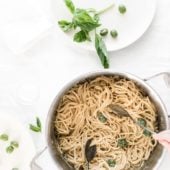 pot of pasta with hands stirring next to a plate with basil and olives
