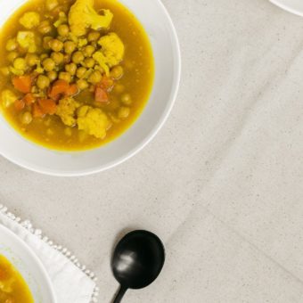 turmeric ginger soup with cauliflower in white bowl beside a black spoon