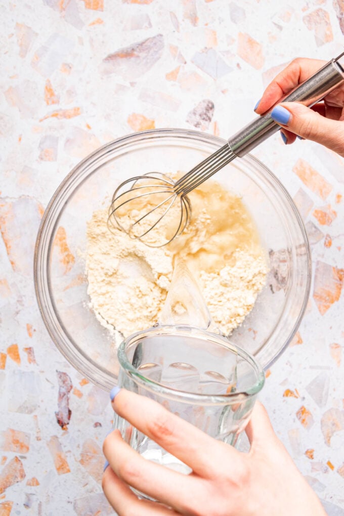 hand adding water to chickpea flour in bowl