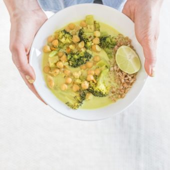 hands holding bowl of chickpea broccoli curry on white background