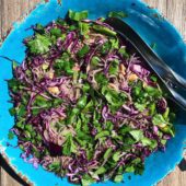 blue bowl of noodle cabbage salad on wood table with spoons