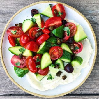 tomato cucumber salad with olives and whipped feta on white plate