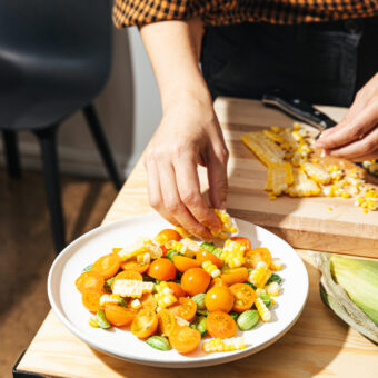 hand tossing tomato and corn salad on plate