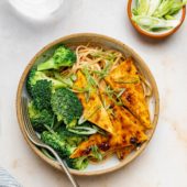 bowl of tofu, broccoli and noodles with glass of water