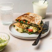 spinach quesadilla on a plate with black fork, jar of pesto and cashew cream