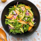 peach and arugula salad in black bowl with spoons