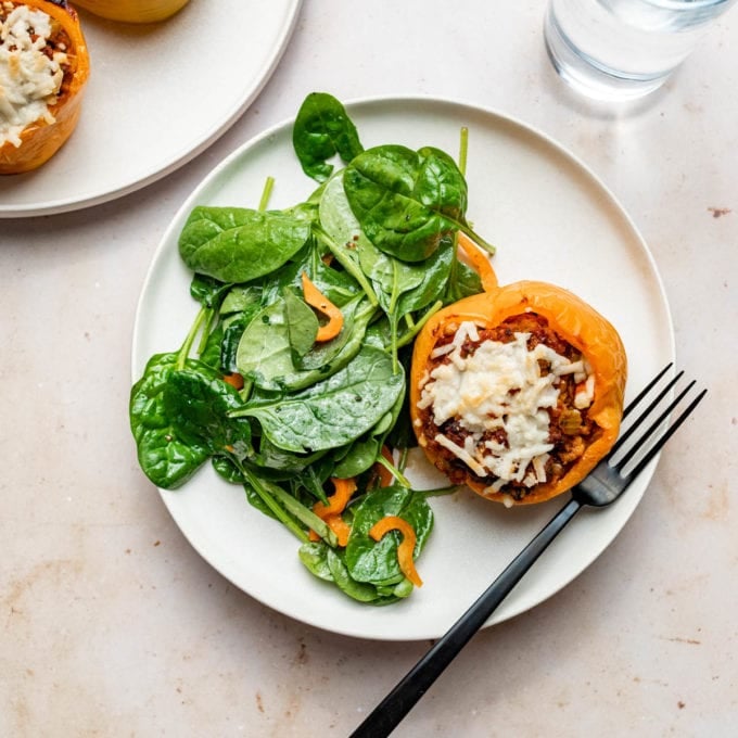 vegan stuffed pepper with spinach salad on white plate with fork