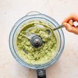 hand stirring broccoli pesto in food processor