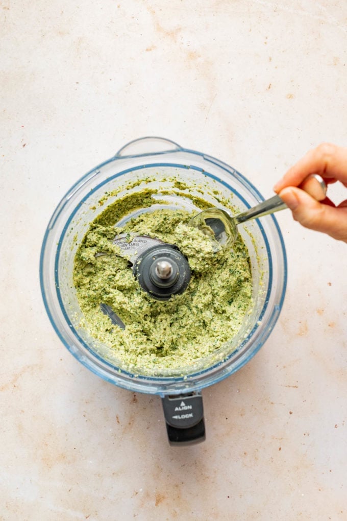 hand stirring broccoli pesto in food processor