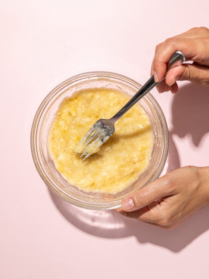 hand mashing banana in glass bowl