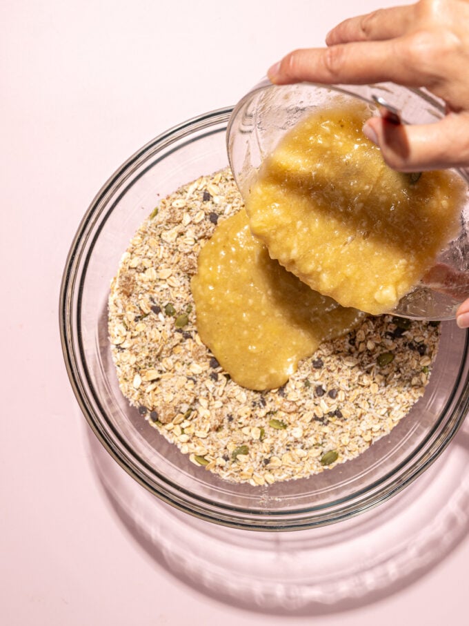 hand pouring mashed banana into bowl of oats