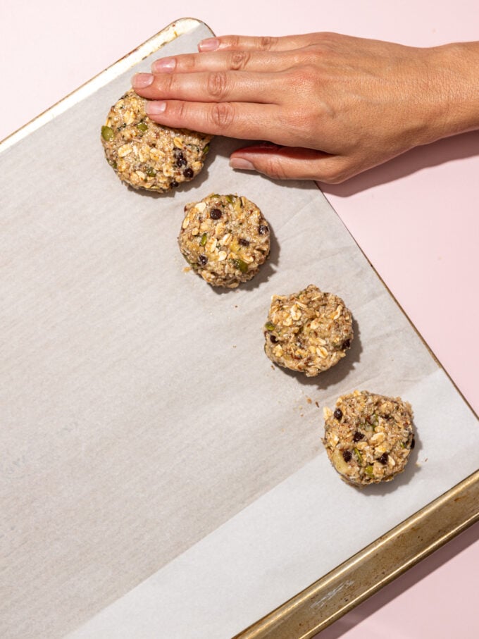 hand pressing oat cookies onto baking sheet