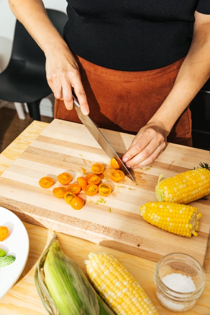 hands cutting tomatoes on wooden cutting board