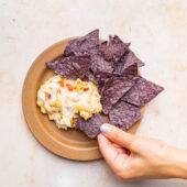 hand dipping chip into vegan corn dip