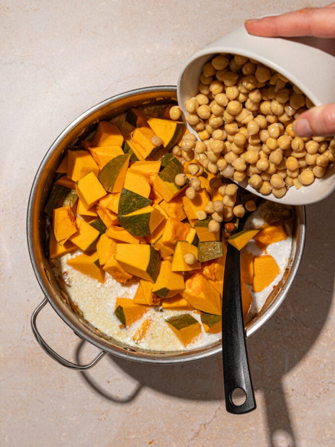 hand pouring chickpeas and kabocha squash into pot