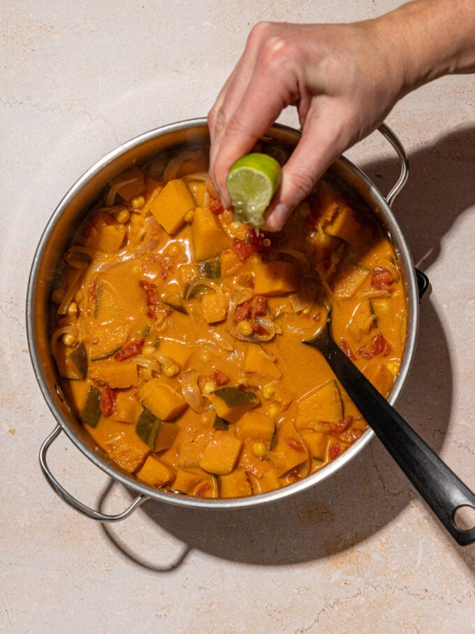 hand squeezing lime into pot of kabocha squash curry