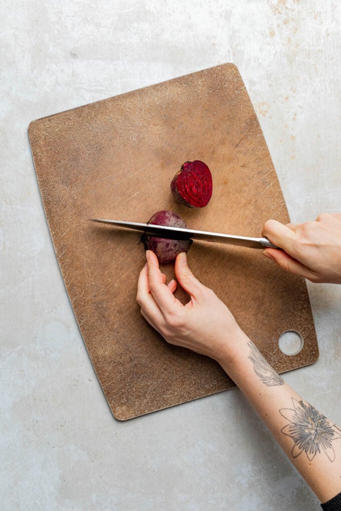 hand cutting beets on wooden cutting board