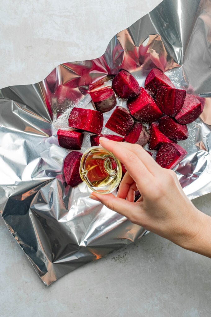 hand pouring oil on beets on tin foil tray