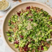 kale quinoa salad in pink bowl with dressing in jar