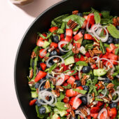 Spinach Salad with Fresh Blueberries and Strawberries in Black Bowl with Dressing in Jar