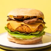 tofu burger stacked with cheese, mushrooms and lettuce on white plate