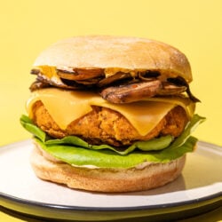 tofu burger stacked with cheese, mushrooms and lettuce on white plate