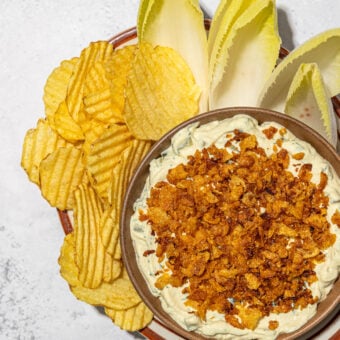 chips, endive and dill pickle dip topped with cornflakes on brown plate