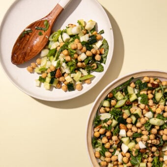Chickpea cucumber salad on white plate with wooden spoon and bowl on yellow background