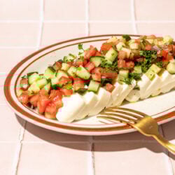 sliced tofu, diced tomato and cucumber on plate with fork on pink tiles