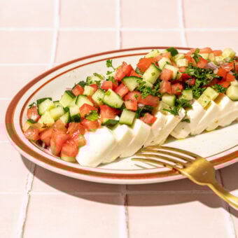 sliced tofu, diced tomato and cucumber on plate with fork on pink tiles