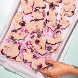 hand grabbing piece of cherry yogurt bark from baking sheet