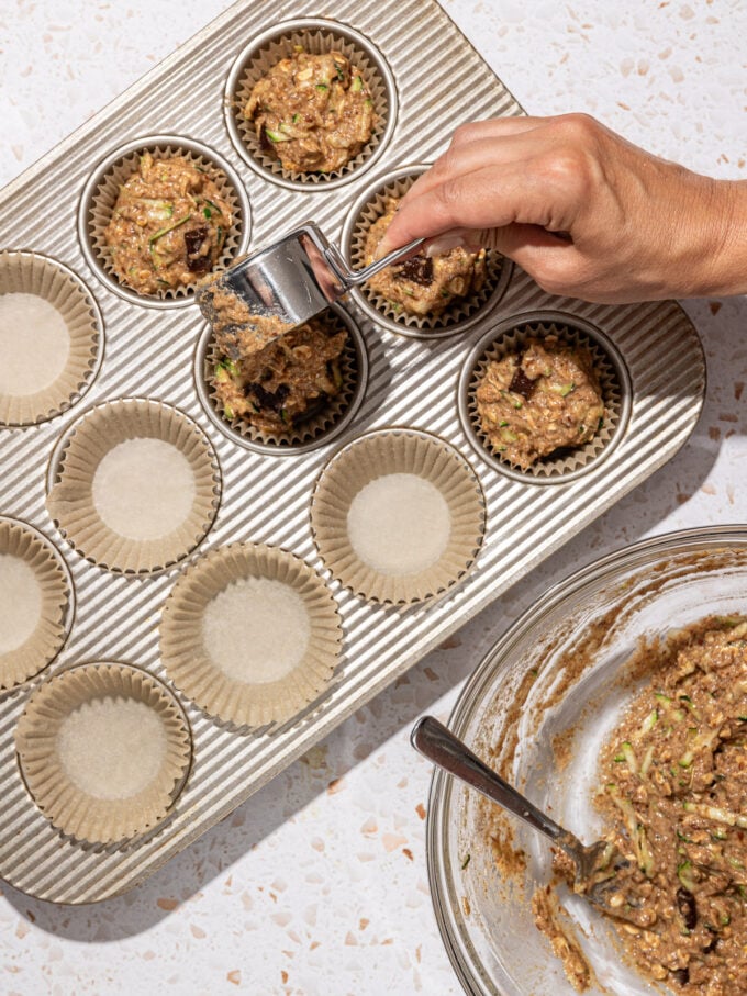 hand pouring muffin batter into muffin pan