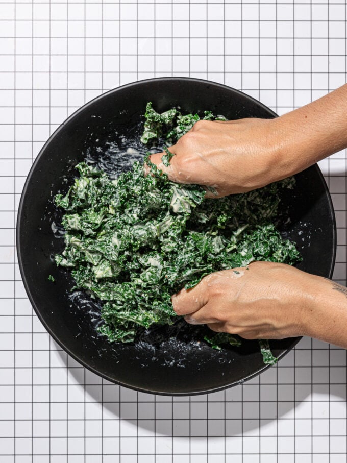 hands massaging kale in black bowl