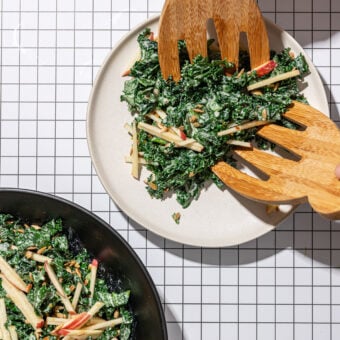 placing kale apple salad on white plate with wooden scoops