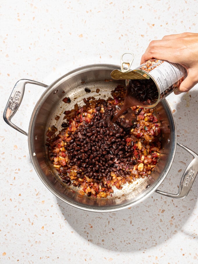 hand pouring can of black beans into soup pot