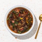 black bean and chard soup in white bowl with gold spoon