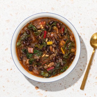 black bean and chard soup in white bowl with gold spoon