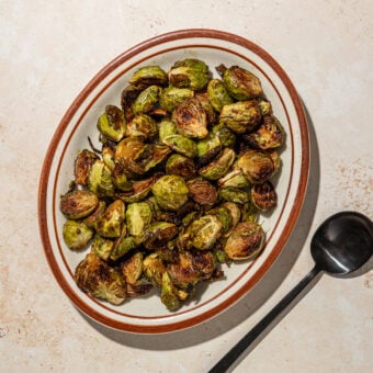 roasted brussels sprouts on a brown plate with black spoon