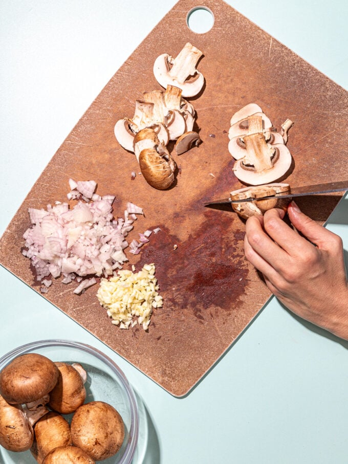 hand slicing mushrooms on cutting board