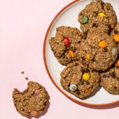 vegan monster cookies piled on a white plate with one cookie to the side missing a bite