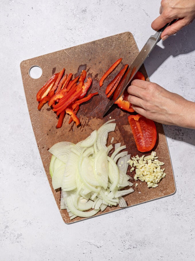 hand slicing red pepper and onion on cutting board