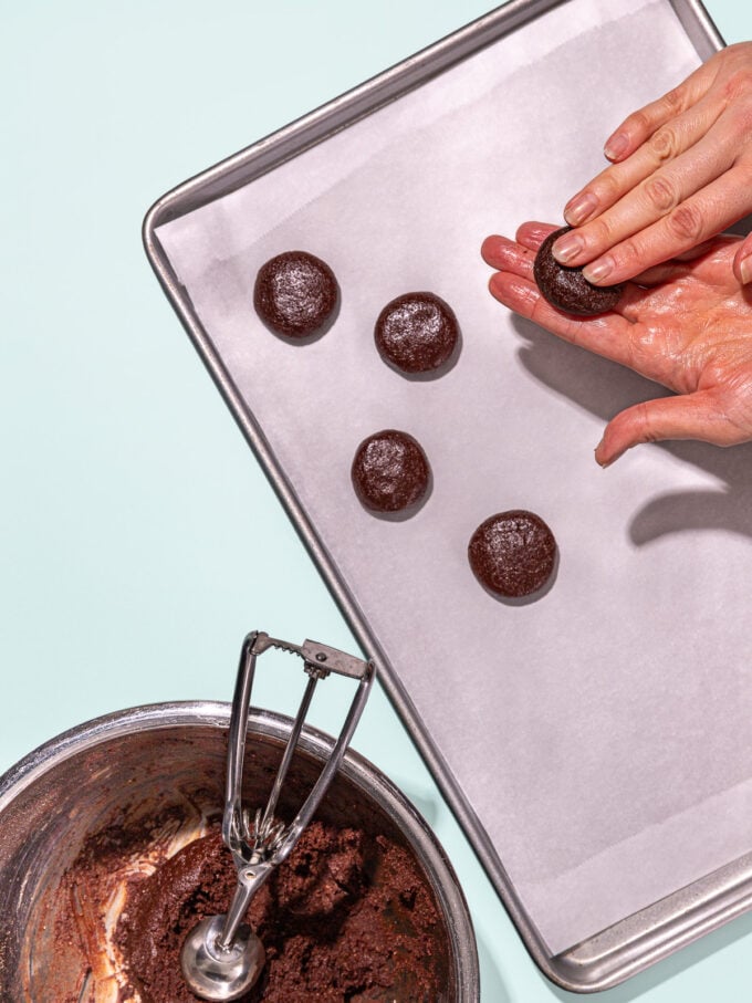 hand pressing mint chocolate cookies over baking sheet with mixing bowl