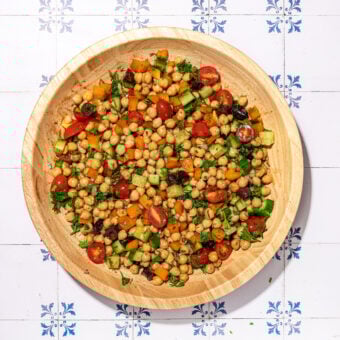 wooden bowl of chickpea salad with cucumber and tomato on white and blue tiled background