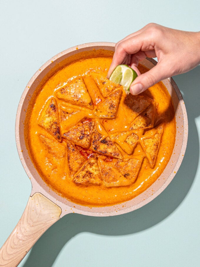 hand squeezing lime into skillet of red curry tofu