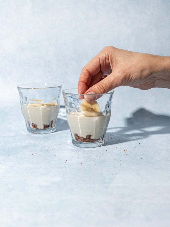 hand adding sliced banana to dessert glasses